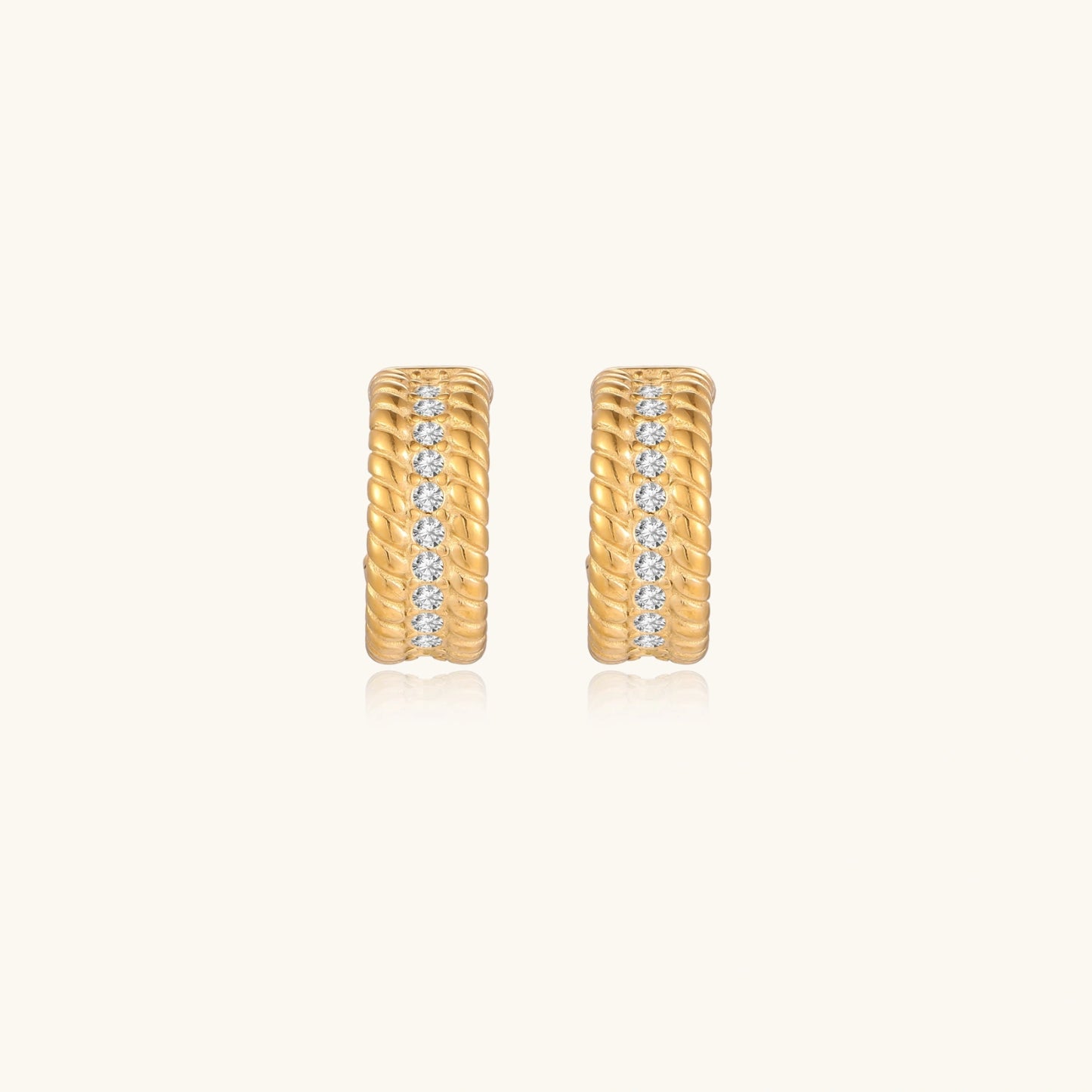 Textured gold huggie hoop earrings with raised ribbed rows creating dimensional sculptural design on cream background