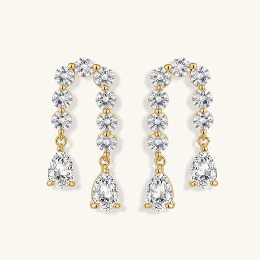 Gold-plated earrings with vertical line of clear crystals and teardrop pendants on neutral background
